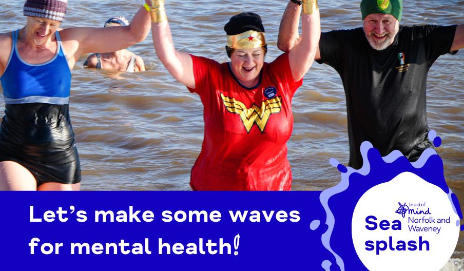 Three adults smiling as they wade out of the sea, holding hands triumphantly. One person is dressed in a Wonder Woman costume, and the others wear swi