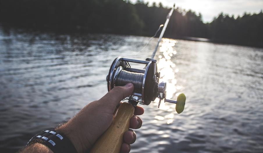 Hand holding a fishing rod over water