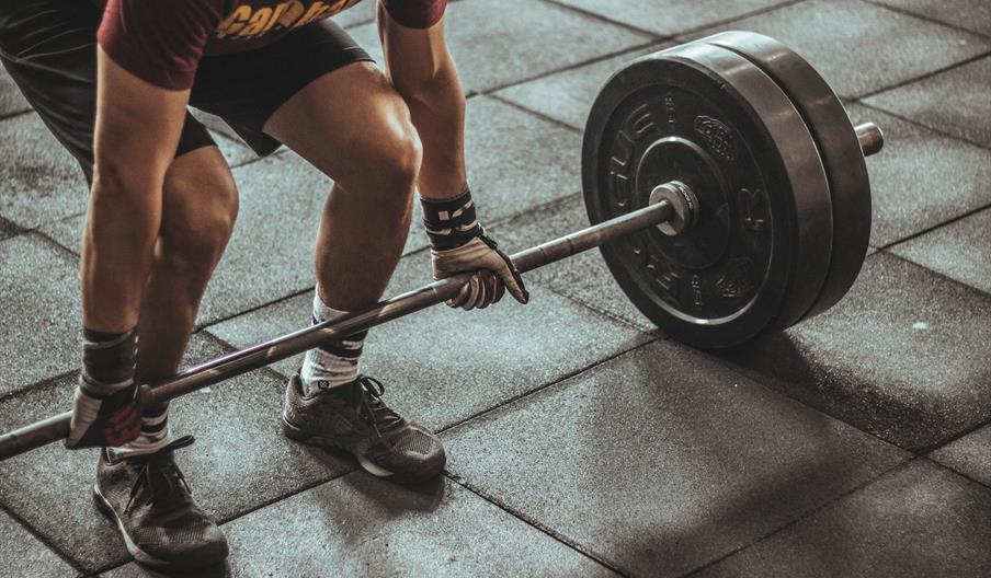 Man in shorts and trainers with gloves on about to lift weight
