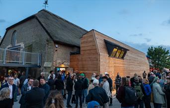 Thatched building with balcony and people gathering outside
