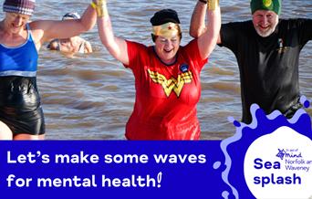 Three adults smiling as they wade out of the sea, holding hands triumphantly. One person is dressed in a Wonder Woman costume, and the others wear swi