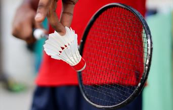 Person holding black badminton racket about to hit shuttlecock