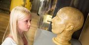 A young girl looking at a model of a head in a display case. The head is looking back at the young girl.