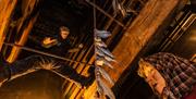 A model of a fisherwoman passing a stick full of fish up to a man standing in the rafters of the smokehouse