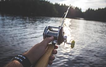 Hand holding a fishing rod over water