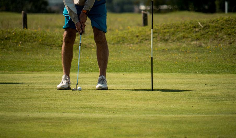 Man in blue shorts about to putt golf ball
